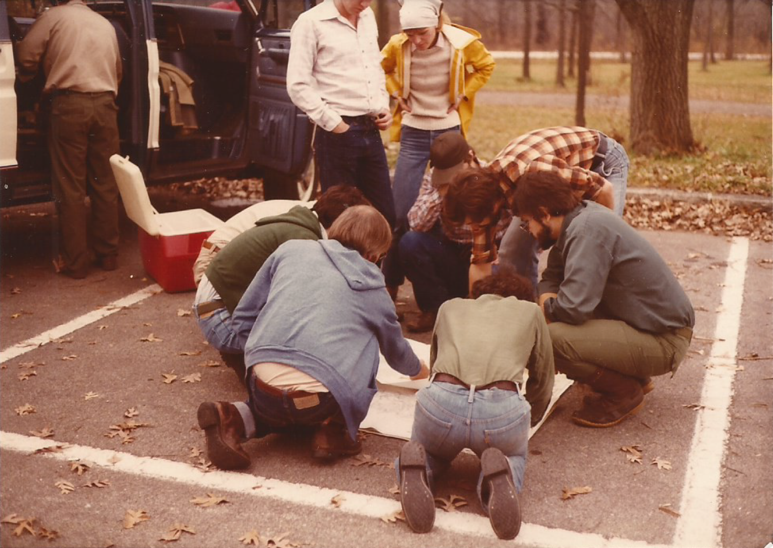 Students crouching and reading a map in a wooded parking lot